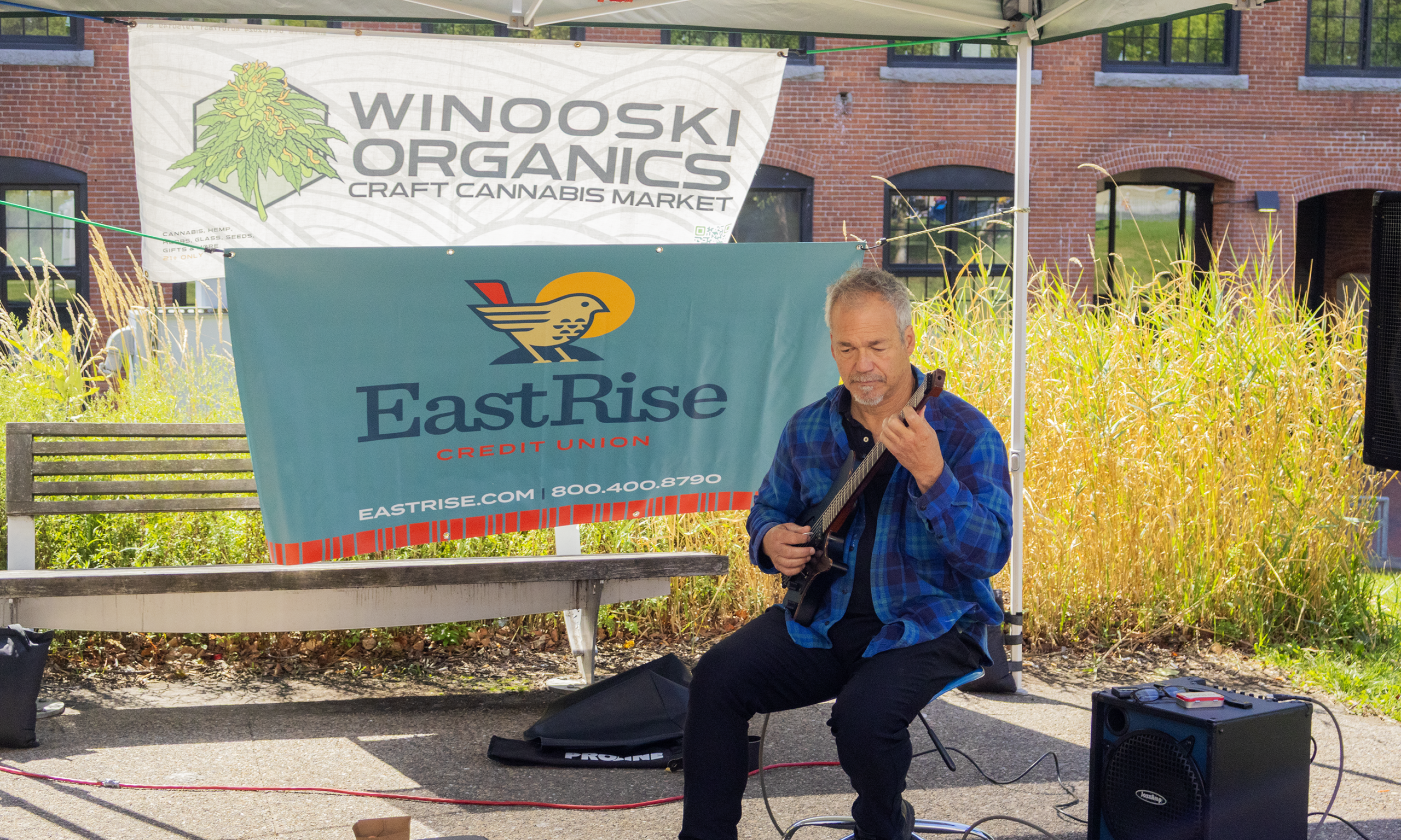 Bob Gagnon playing in front of sponsorship banners at the Winooski Farmers Market